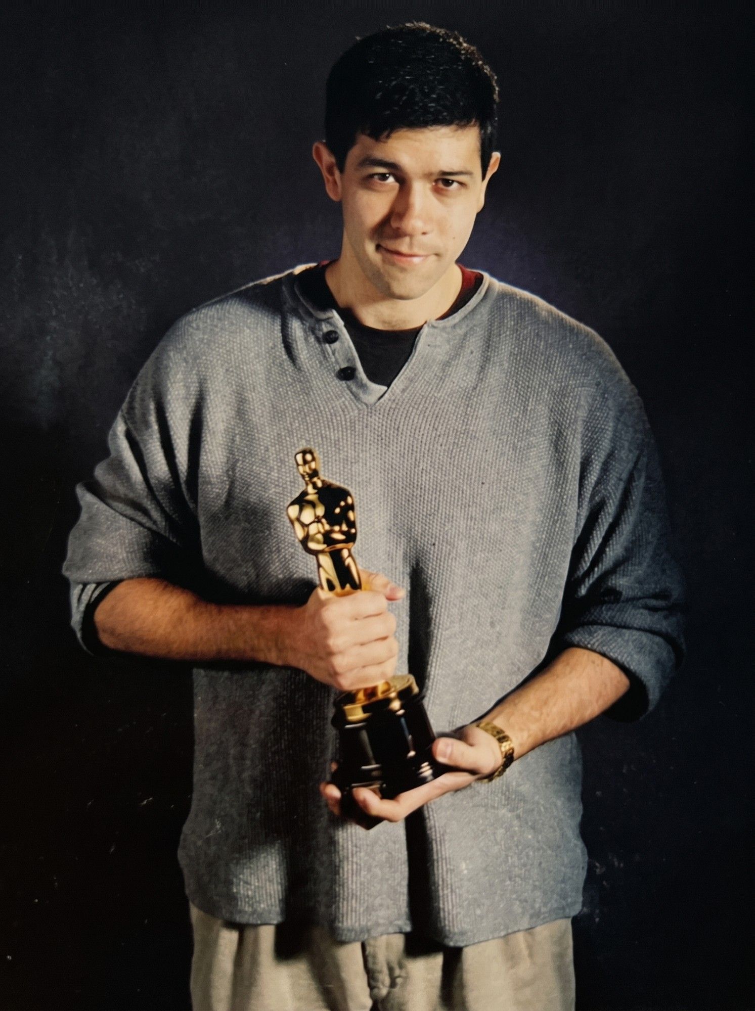 A young Darin Grant in a grey sweater holding an Academy Award statuette against a dark backdrop