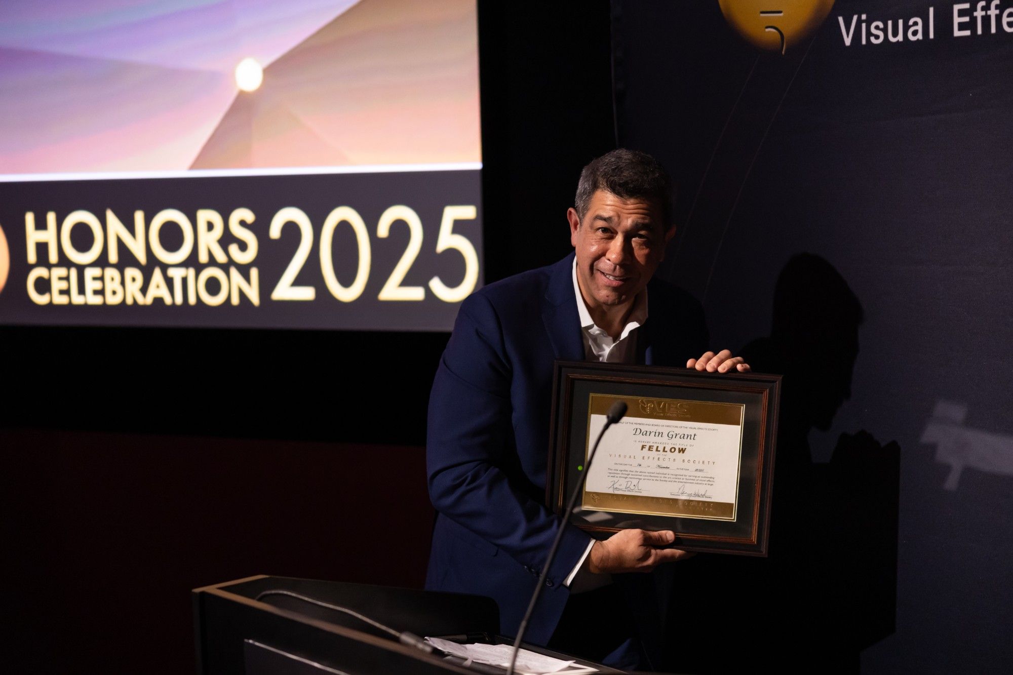 Darin Grant on stage holding his framed VES Fellow certificate at the VES Honors Celebration 2025
